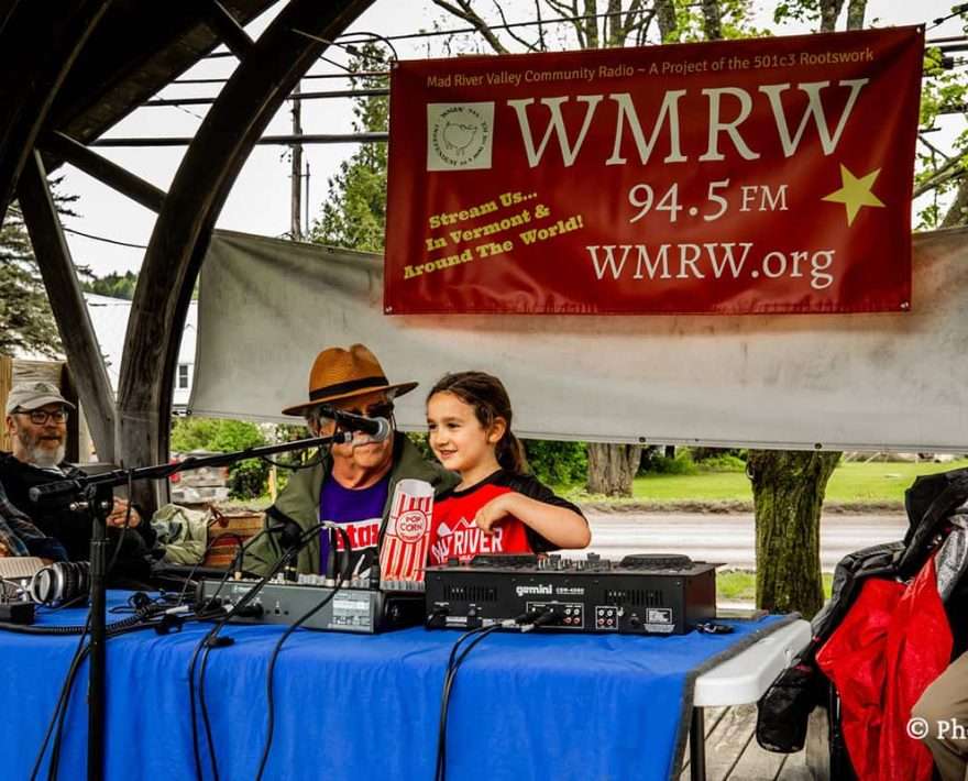 A litttle girl sitting at a table for a local radio station at a Vermont Farmers Market in Waitsfield